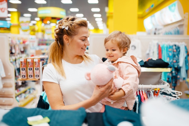 Madre con la sua piccola figlia che sceglie il cane della peluche nel negozio per bambini.