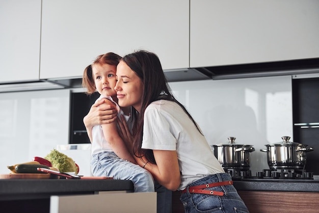 Madre con la sua piccola figlia che si abbracciano al chiuso in cucina