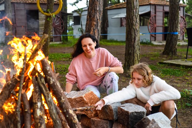 Madre con le figlie che trascorrono del tempo insieme accendono un fuoco e lanciano bastoni