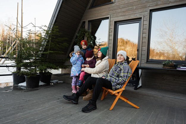 Madre con quattro bambini si siedono sulla terrazza fuori dalla griglia piccola casa in montagna