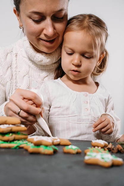 Madre con ragazza che decora i biscotti di pan di zenzero per natale
