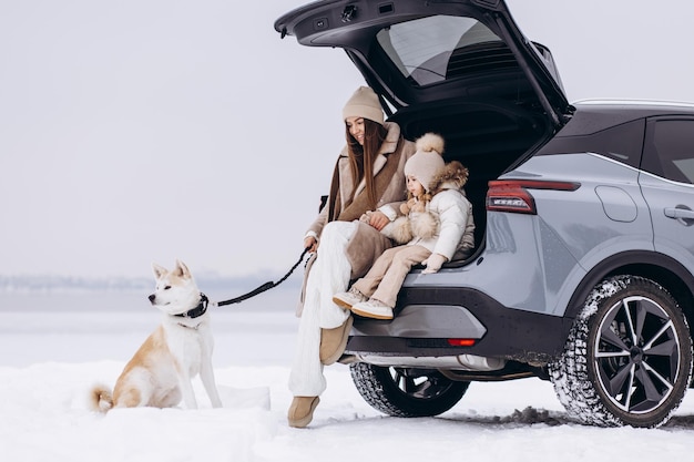 Madre con sua figlia e il loro cane seduti nel bagagliaio di una macchina in un clima invernale