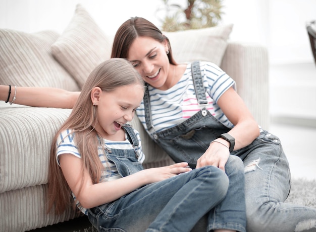 Madre con una piccola figlia che utilizza uno smartphone seduto nel nuovo soggiorno