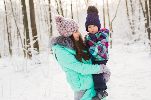 Madre di famiglia felice e figlia della neonata che giocano e ridono in inverno all'aperto nella neve.