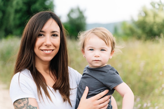 Madre e bambina che guardano la macchina fotografica mentre si abbracciano all'aperto