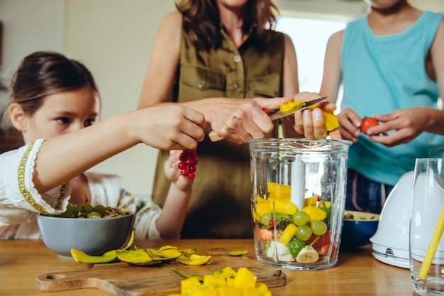 Madre e bambini che mettono la frutta in un frullatore per frullati