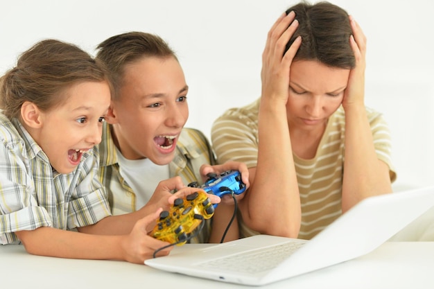 Madre e bambini seduti al tavolo con il computer portatile che giocano