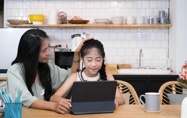 Madre e bambino asiatico bambina che impara e guarda il computer portatile che fa i compiti studiando con il sistema di elearning per l'istruzione onlinevideoconferenza per bambini con tutor insegnante a casa