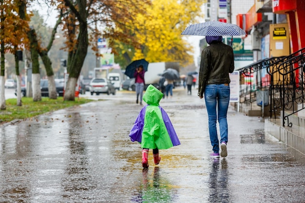 Madre e bambino camminano in città con un ombrello sotto la pioggia