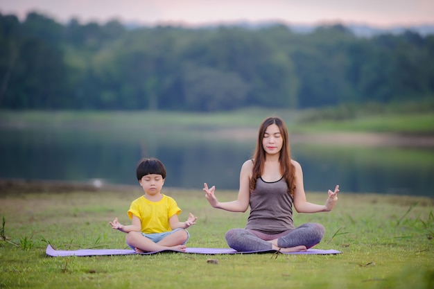 Madre e bambino che fanno esercizi di yoga sull'erba al parco prima del tramonto in estate.