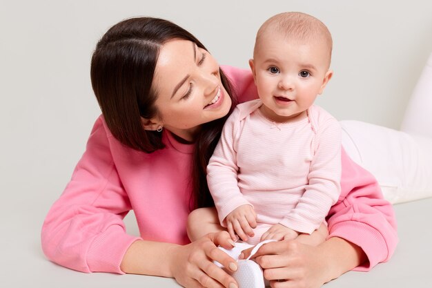 Madre e bambino che giocano insieme, bambino carino seduto sul pavimento che indossa una tuta, mamma che abbraccia il suo bambino e la guarda con amore e sorriso gentile, famiglia felice.