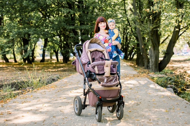 Madre e bambino della bella e giovane donna in un passeggiatore che camminano nel parco