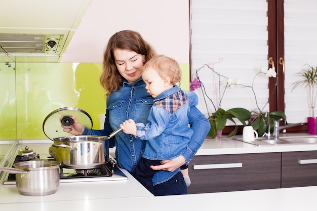 Madre e bambino in braccio che cucinano la cena in cucina. La mamma e il suo bambino cucinano la zuppa insieme