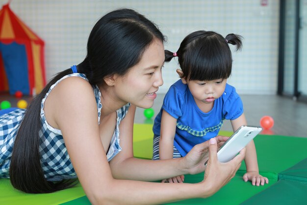 Madre e carina bambina asiatica giocando uno smartphone e posa nella stanza del bambino