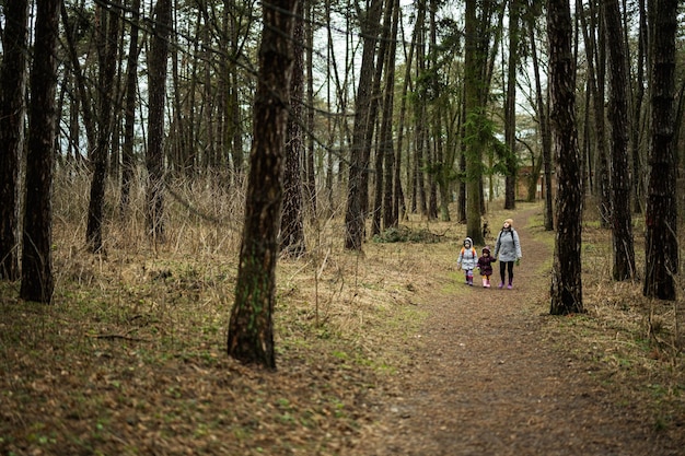 Madre e due figlie con zaini che camminano insieme lungo la strada forestale