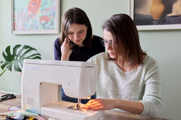 Madre e figlia adolescente cuciono insieme a casa. La mamma insegna alla figlia a cucire sulla macchina, le donne cuciono i giocattoli e i vestiti per i giocattoli. Genitore e adolescente, relazioni, stile di vita, creatività, abilità