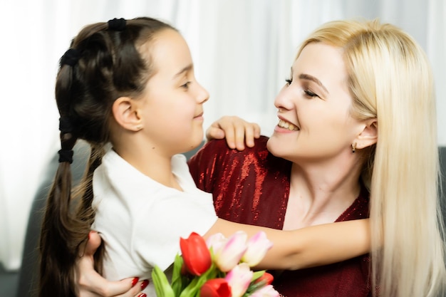 Madre e figlia allegre attraenti alla moda che si godono le vacanze insieme con un grande bouquet colorato stagionale impeccabile di tulipani, concetto di piacere di gioia di piacere di comfort su sfondo grigio