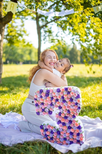 Madre e figlia allegre che si divertono per il compleanno del bambino su una coperta con decorazioni di carta nel parco