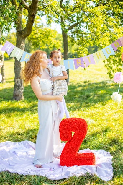 Madre e figlia allegre che si divertono per il compleanno del bambino su una coperta con decorazioni di carta nel parco