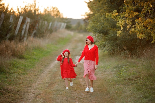 Madre e figlia camminano insieme in un meleto vestiti rosso vivo sottolineano tutta la bellezza