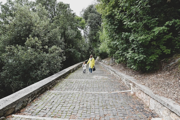 Madre e figlia camminano sul sentiero attraverso la bellissima foresta autunnale Donna e bambina camminano attraverso un sentiero in salita in una foresta Avventura Stile di vita attivo Percorso di vita dei genitori