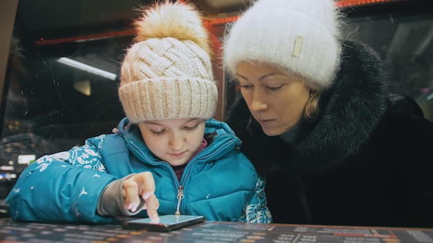 Madre e figlia caucasiche attraenti che usano lo smartphone seduti al bar Il bambino piccolo avanzato mostra e spiega alla mamma qualcosa sullo smartphone