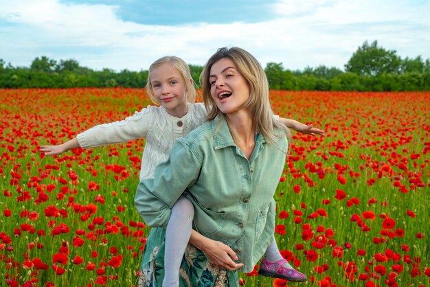 Madre e figlia che camminano attraverso un campo di papaveri in fiore bambino e mamma cavalcano sulle spalle in estate p