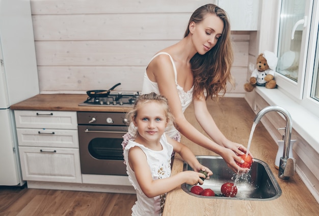 Madre e figlia che cucinano e che lavano le verdure in cucina