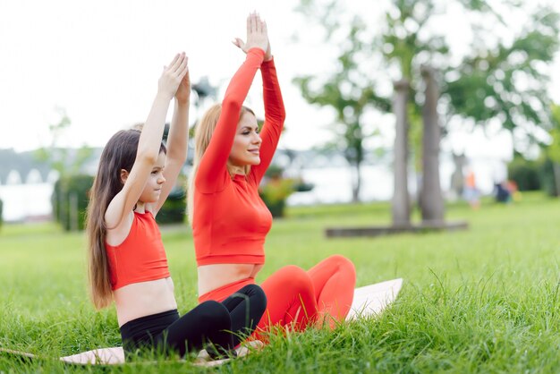 Madre e figlia che fanno esercizi di yoga sull'erba nel parco durante il giorno