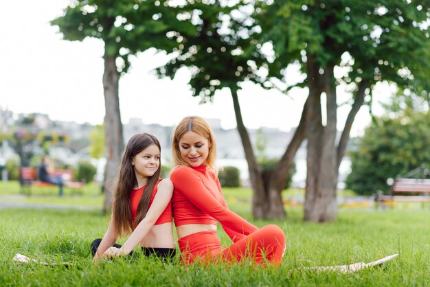 Madre e figlia che fanno esercizi di yoga sull'erba nel parco durante il giorno