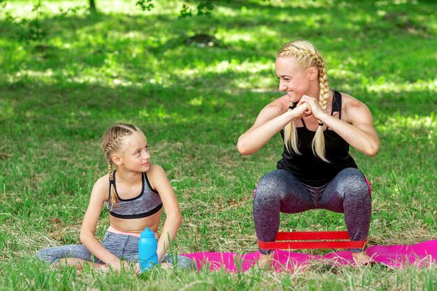 Madre e figlia che fanno esercizi sportivi sul tappeto nel parco all'aperto