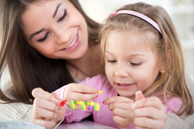 Madre e figlia che giocano a casa. Stanno facendo braccialetti di perline.