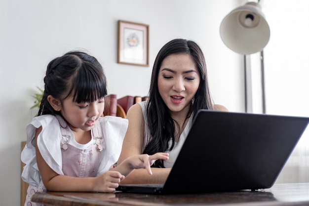 Madre e figlia che giocano insieme computer portatile nel salone a casa.