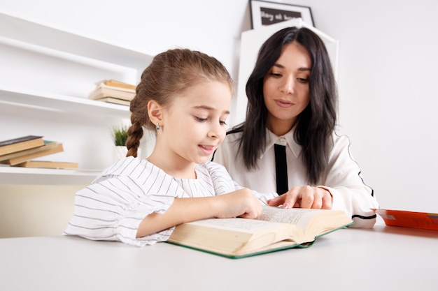 Madre e figlia che leggono seduti a casa al tavolo.