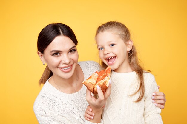 Madre e figlia che mangiano pizza insieme e divertendosi isolata sulla stanza gialla.