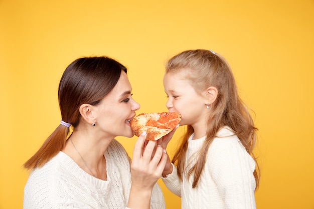 Madre e figlia che mangiano pizza insieme e divertirsi isolato sopra lo studio giallo.