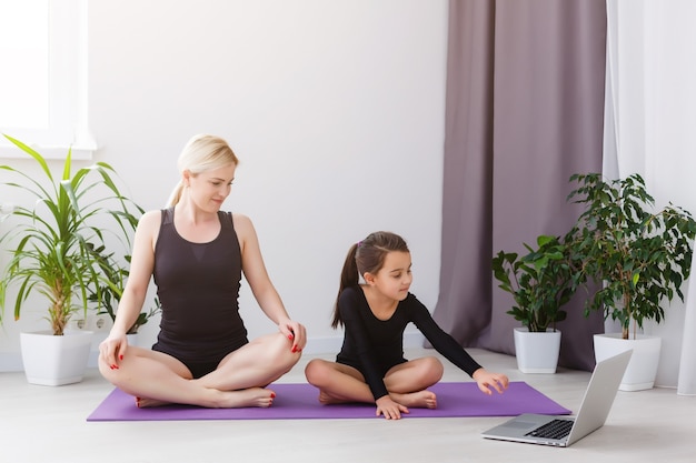 Madre e figlia che praticano lezioni di yoga online a casa durante il periodo di isolamento in quarantena durante la pandemia di coronavirus. Famiglia che fa sport insieme online da casa. Uno stile di vita sano
