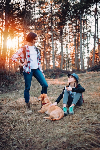 Madre e figlia che riposano con il cane in foresta durante il tramonto