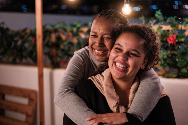 Madre e figlia che si abbracciano sorridendo una notte sulla terrazza e si godono lo stile di vita del concetto sorrisi divertenti