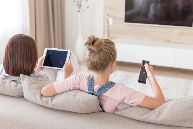 Madre e figlia che si siedono sullo strato che guardano TV in salone