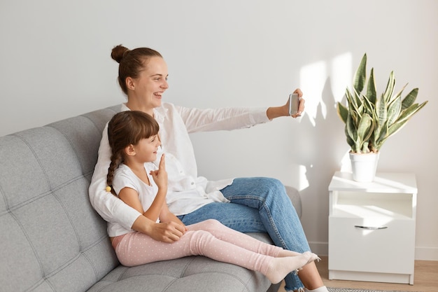 Madre e figlia di famiglia emotiva che si fanno selfie o trasmettono in livestream, fanno videochiamate e mostrano il segno v alla telecamera, esprimendo positività e ottimismo.