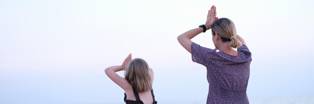 Madre e figlia fanno yoga meditano nella posizione del loto sulla spiaggia