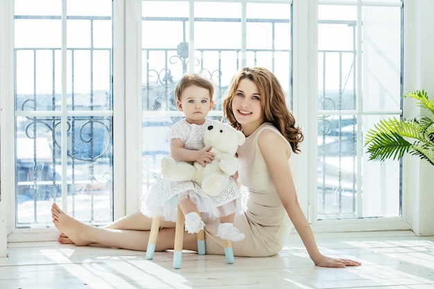 Madre e figlia felice e bella casa insieme giocando sul pavimento sullo sfondo della finestra