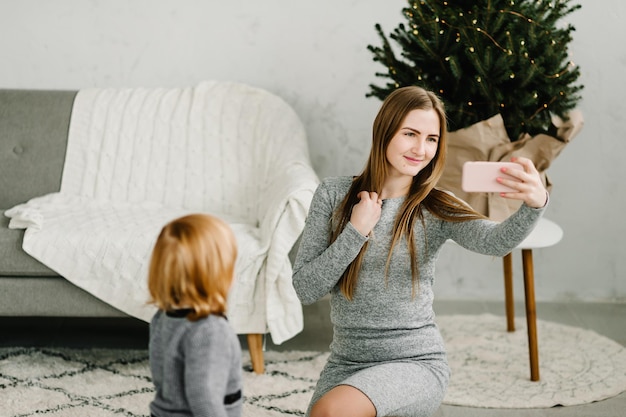 Madre e figlia felici parlano in videochiamata con i parenti al telefono La giovane mamma e il bambino vengono fotografati o scattano selfie vicino all'albero di Natale Buon Natale e buone feste