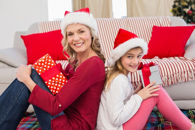 Madre e figlia festive che sorridono alla macchina fotografica con i regali