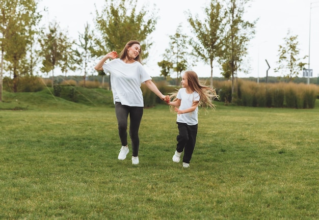 Madre e figlia giocano e corrono per il parco in una bella giornata in cui la famiglia si diverte nel parco sull'erba facendo jogging mattutino