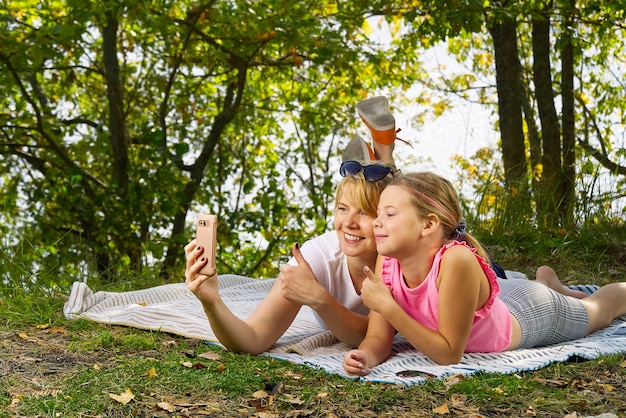 Madre e figlia giocano su una coperta nella foresta di autunno vicino al fiume o al lago. Giovane madre che gioca con la figlia in autunno parco il giorno pieno di sole