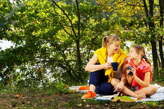 Madre e figlia giocano su una coperta nella foresta di autunno vicino al fiume o al lago. Giovane madre che gioca con la figlia in autunno parco il giorno pieno di sole