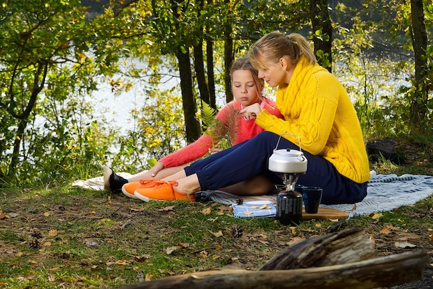 Madre e figlia giocano su una coperta nella foresta di autunno vicino al fiume o al lago. Giovane madre che gioca con la figlia in autunno parco il giorno pieno di sole