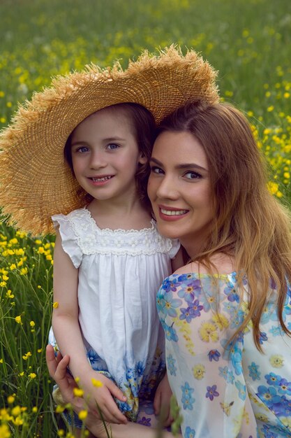 Madre e figlia in abiti e cappello stanno in un campo di fiori gialli nel giorno d'estate